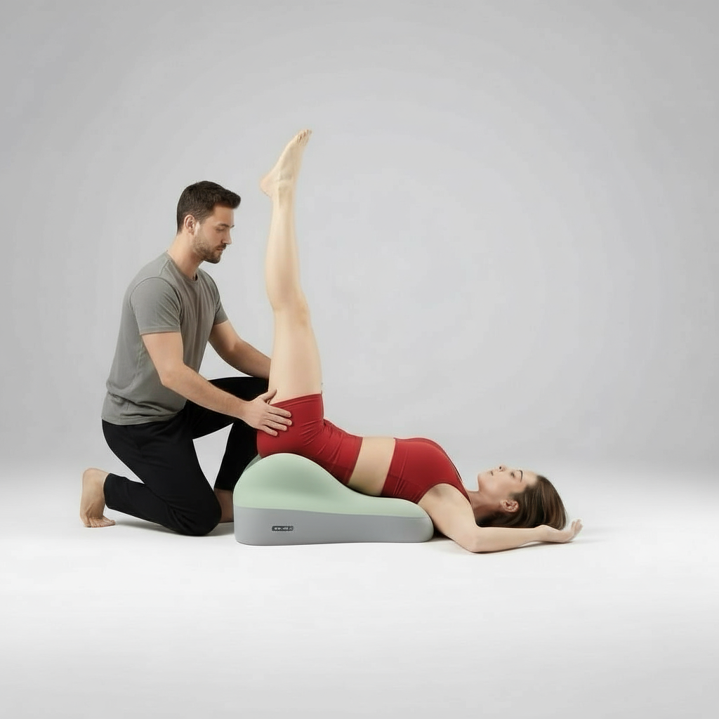 A woman lies on her back on the Todle Couple Pillow, raising her legs vertically as a man in athletic wear kneels beside her, assisting and guiding her during the exercise. Both are dressed in athletic clothing.